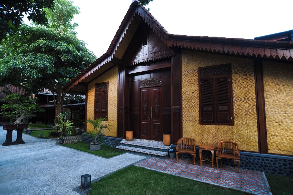 A traditional wooden house with a tiled entrance and a small porch with chairs.