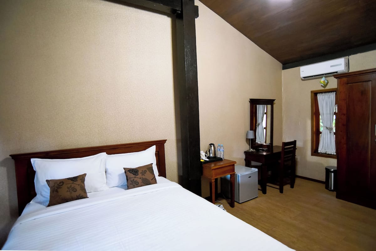 Habitación de hotel con cama, escritorio, silla, refrigerador pequeño, espejo y aire acondicionado.