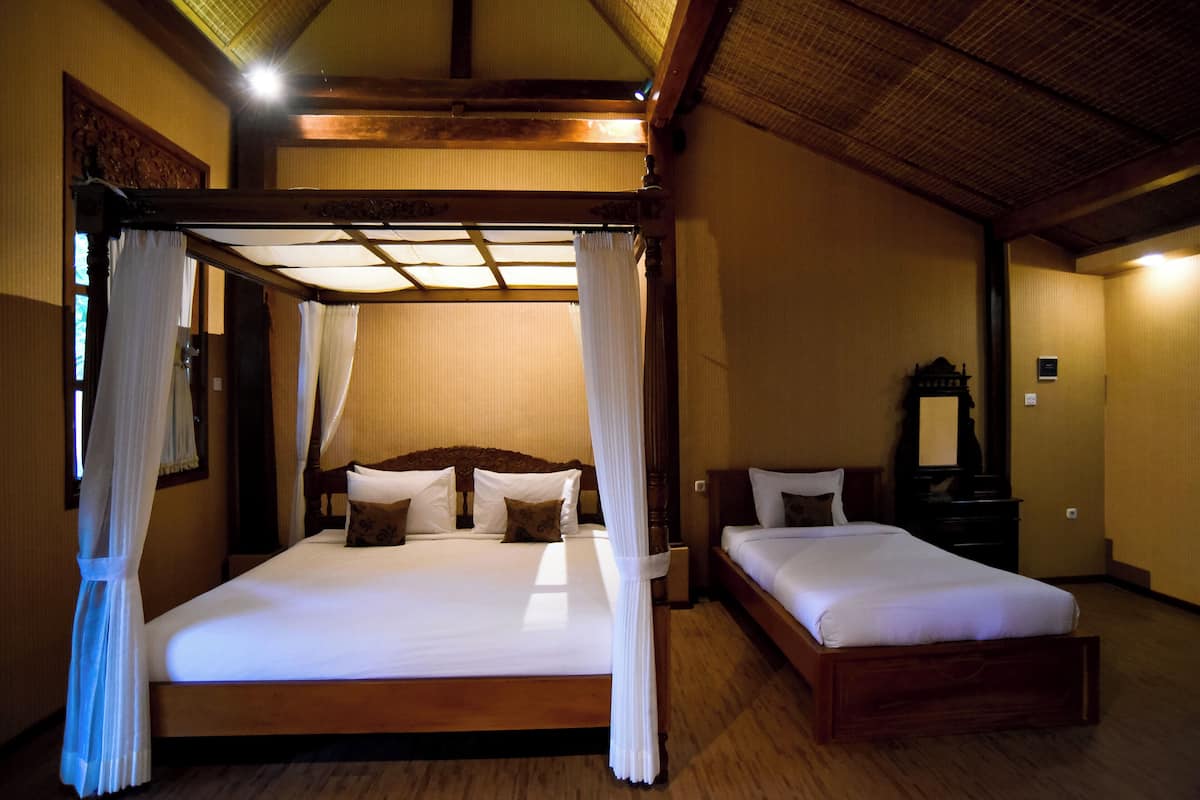 Una cama doble con dosel, una cama individual más pequeña, suelo de madera y un cabecero de madera tradicional.