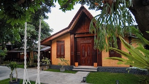 A traditional wooden house with a tiled roof, a stone pathway, and a small garden with a palm tree. - Ndalem Mataram (Banyuwangi)