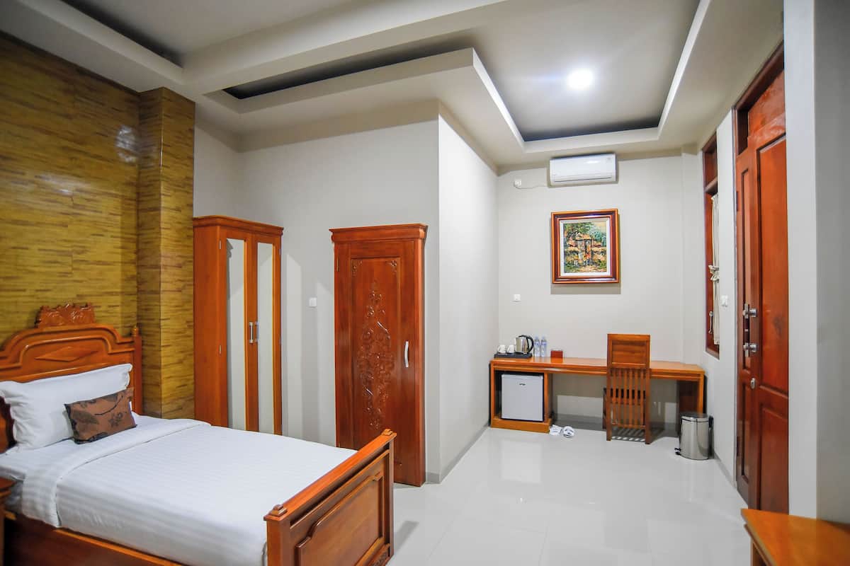Una habitación de hotel con cama, escritorio, silla, un refrigerador pequeño y un cubo de basura.