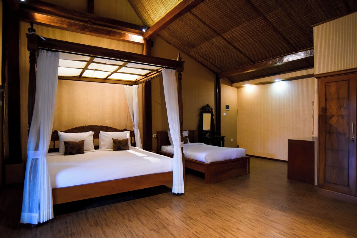 A four-poster bed with white bedding and a canopy, a smaller bed, a wooden wardrobe, and a mirror on the wall.