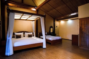 A four-poster canopy bed with a wooden frame and white bedding, a wooden floor, and a traditional room layout with a wardrobe and a mirror. - Ndalem Mataram (Banyuwangi)