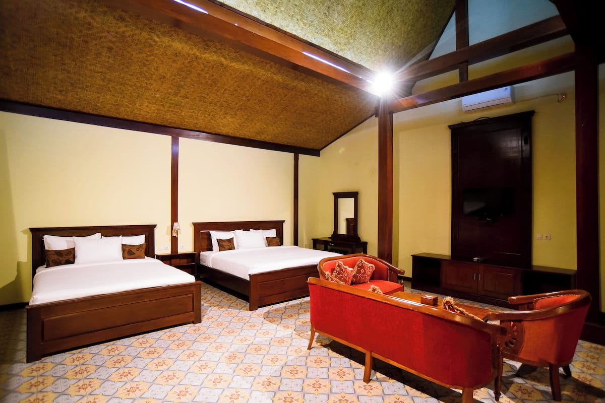 Habitación de hotel con dos camas, un sofá rojo, un armario de madera y un televisor.