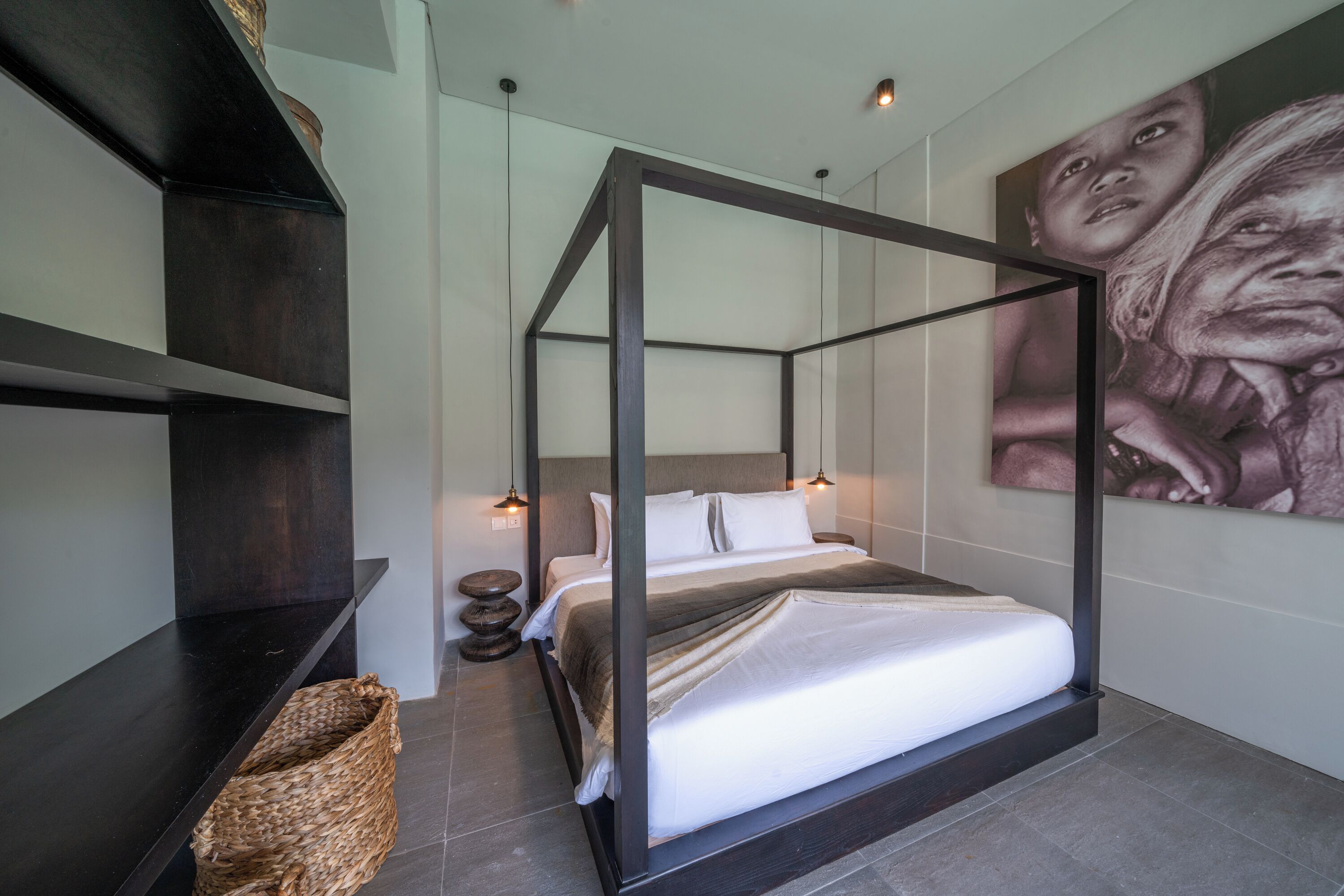 A modern bedroom with a four-poster bed, a large wall art piece, and a woven basket on a dark wooden bench.