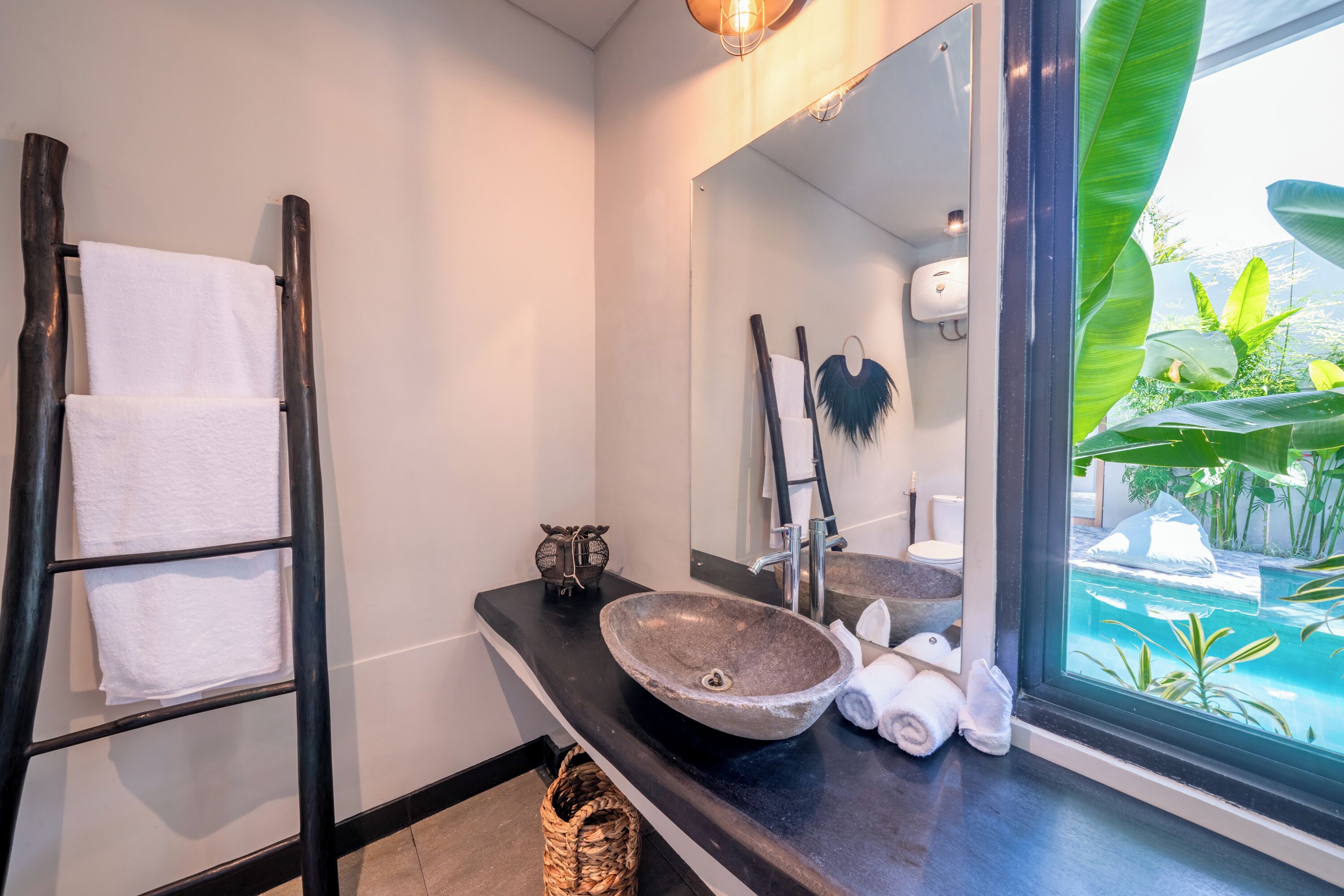 A bathroom with a black towel rack, a stone sink, a mirror, and a view of a pool through a window.
