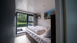 Een slaapkamer met een groot raam met uitzicht op een waterpartij, een bed en een schilderij aan de muur.