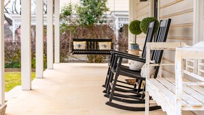 Un porche abrité avec un banc et une table, des colonnes blanches et un pot de fleurs.