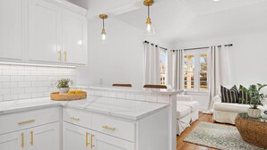 Une cuisine moderne avec des meubles blancs, des poignées dorées et des luminaires suspendus.