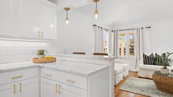 A modern kitchen with white cabinetry, gold handles, and pendant lighting.