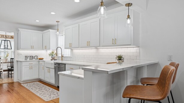 Une cuisine moderne avec des meubles blancs, un îlot central, des luminaires suspendus et un pare-feu apparent.