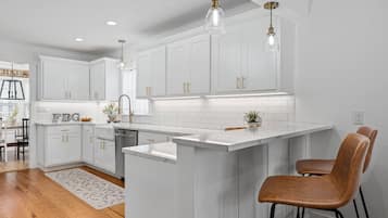 A modern kitchen with white cabinetry, a central island, pendant lighting, and a visible backsplash.