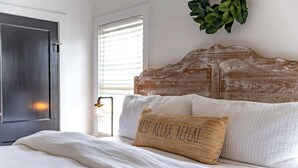 Une chambre à coucher avec une tête de lit en bois, une literie blanche et un coussin tissé orné de motifs.