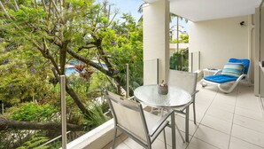 Ein Balkon mit Tisch und Stühlen, mit Blick auf einen Pool und üppiges Grün.