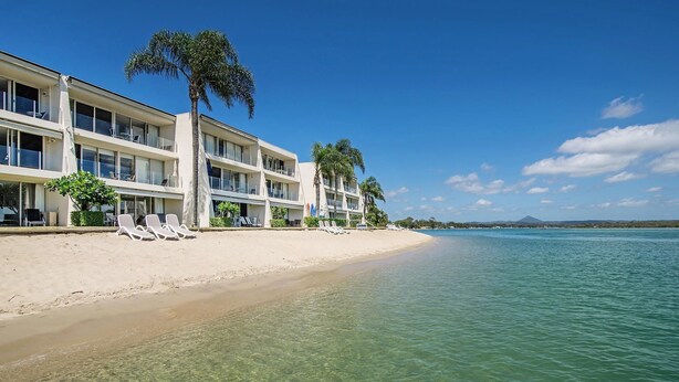 Ein Strandhotel mit klarem Wasser, Palmen und Liegestühlen.