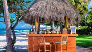 Un bar de playa con dos sillas de madera, techo de paja y vista al océano.