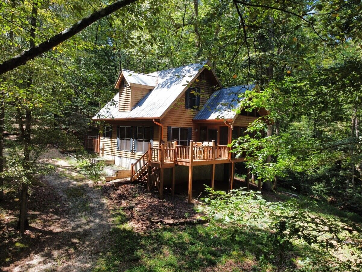 Una cabaña de madera con terraza, rodeada de un bosque denso.
