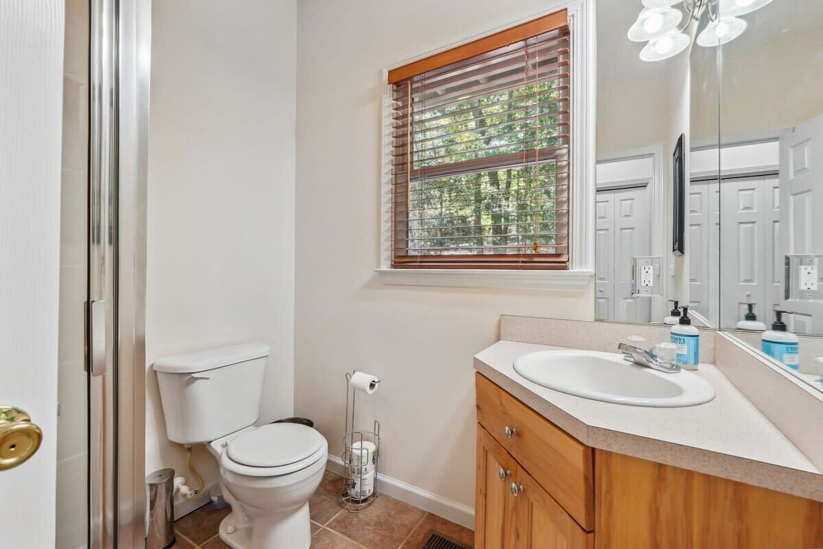 A bathroom with a toilet, sink, and window with blinds.