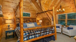 Een slaapkamer in een blokhut met een hemelbed, twee nachtkastjes en een raam met uitzicht op het bos.