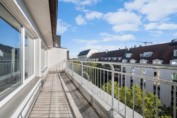 A balcony with a tiled floor, white railings, and a view of neighboring buildings and a construction crane in the background.