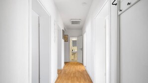 A narrow hallway with white walls and wooden flooring, leading to a bathroom with a sink and mirror. - Munich Gem - 2 Bedroom Alpine View Tranquility (München)