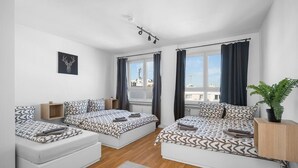 A modern, well-lit bedroom with two beds, a large window with curtains, a potted plant, and a city view. - Munich Gem - 2 Bedroom Alpine View Tranquility (München)