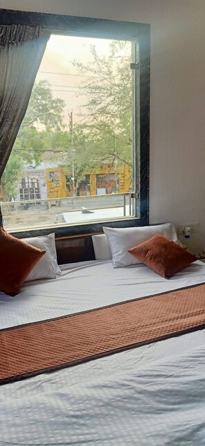 A hotel room with a bed, pillows, a window, and a view of the outside. - BRAJDHAM HOTEL BARSANA (Chhata)