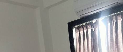 Quarto de hotel com cama, janela com cortinas e aparelho de ar condicionado.