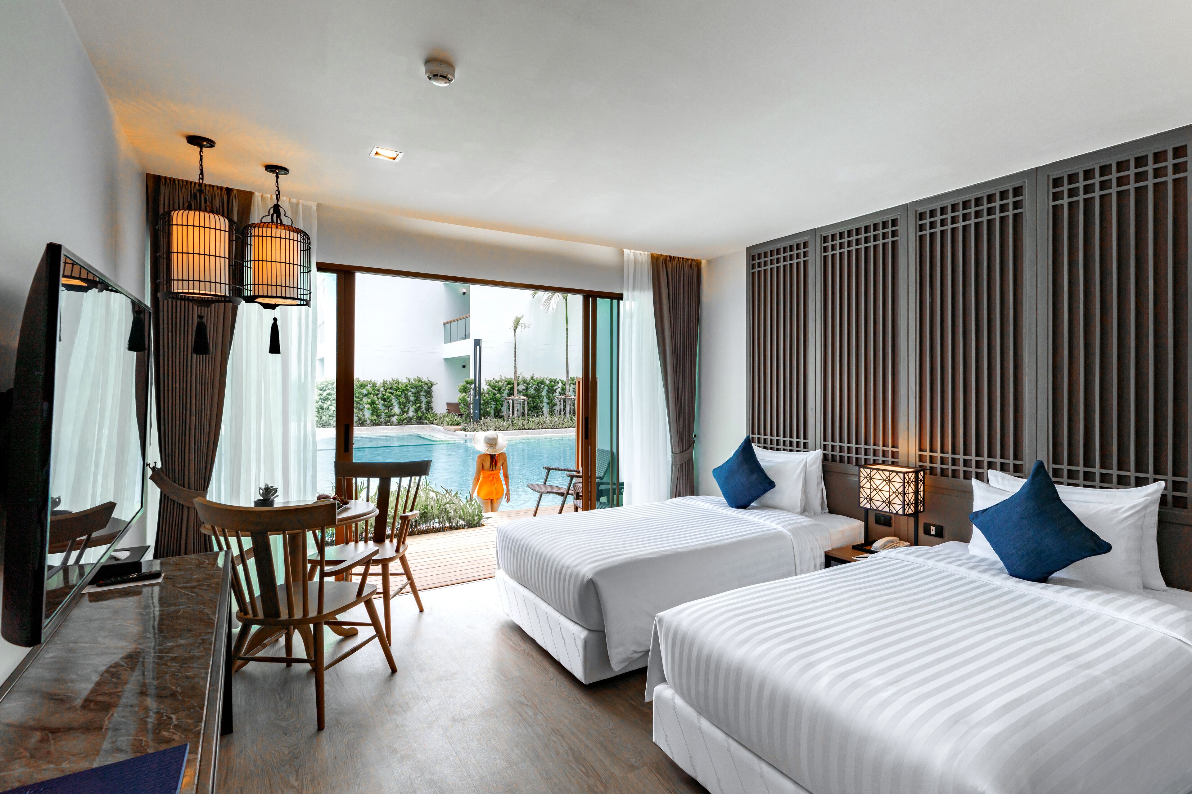 Une chambre d’hôtel avec deux lits, un coin repas, une vue sur la piscine et une grande fenêtre.