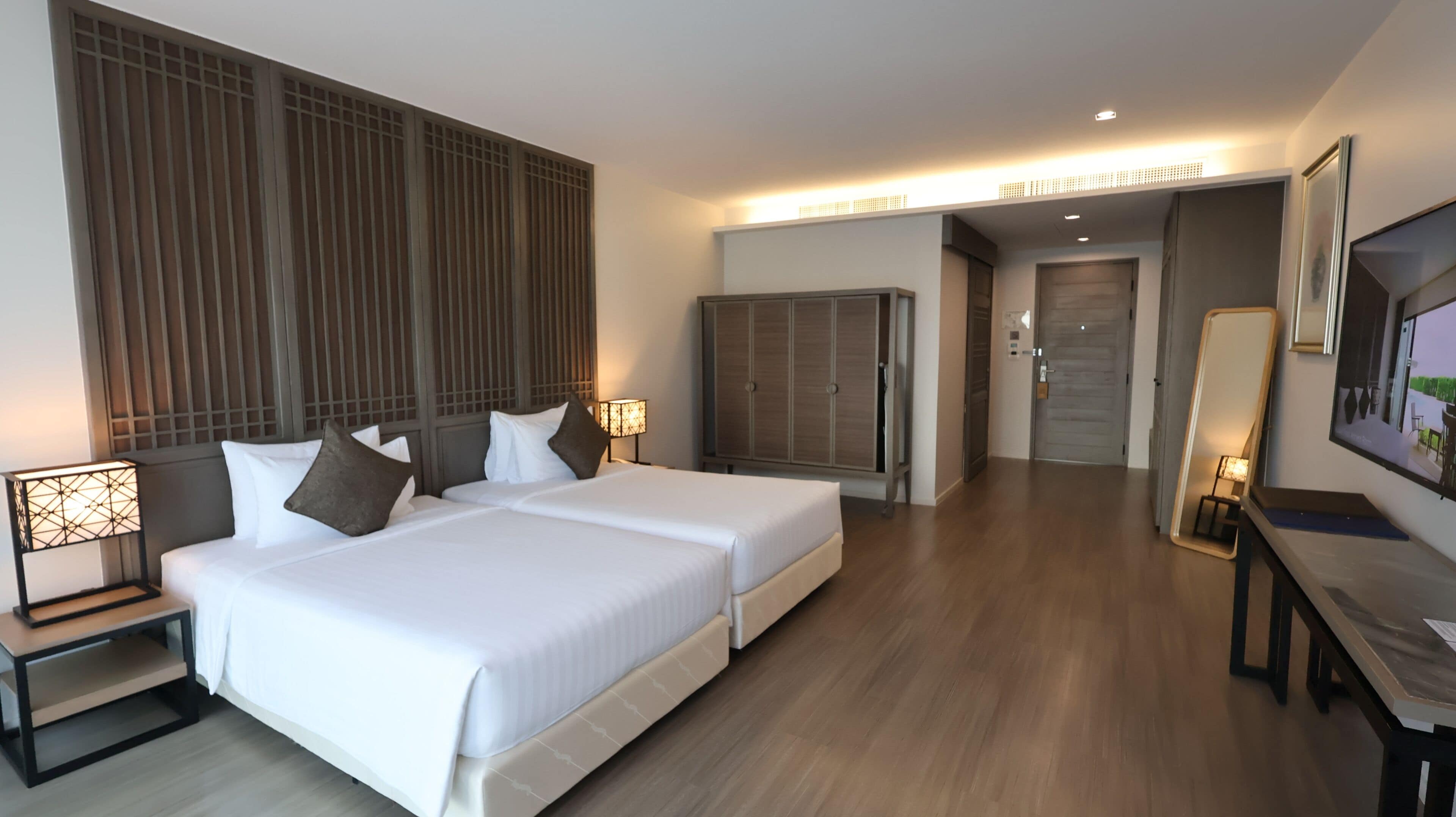 A hotel room with a large bed, bedside tables, a wardrobe, a desk, and a television.