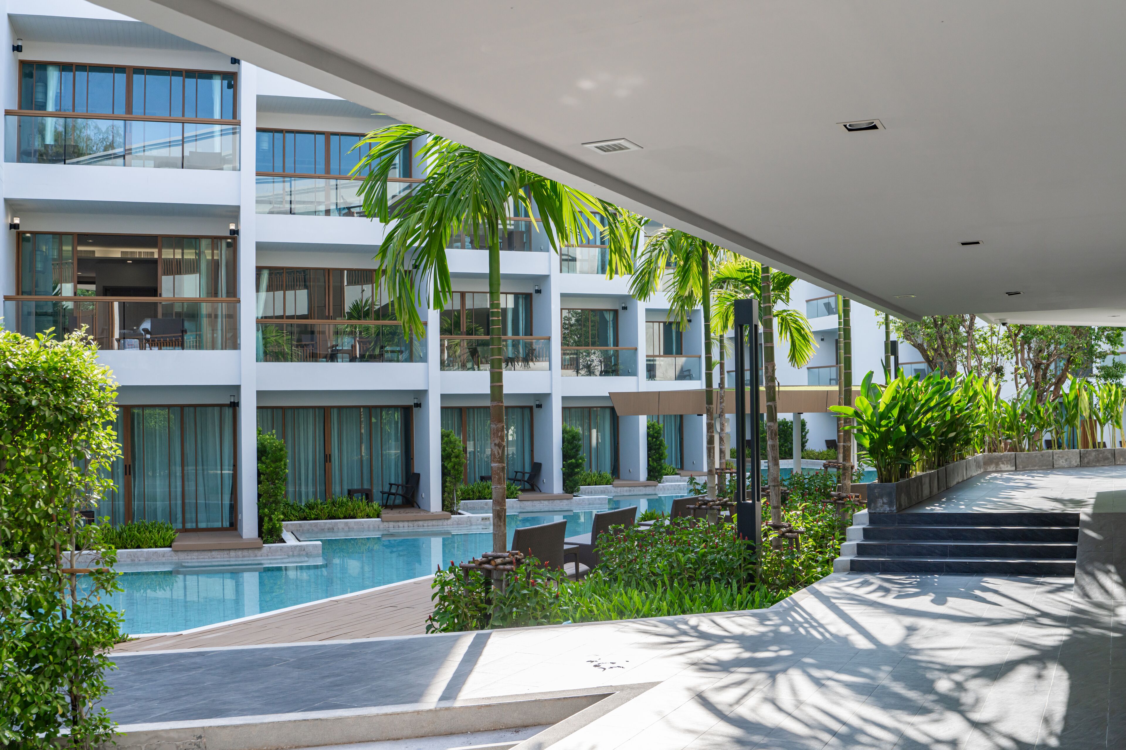 Un hotel moderno con piscina, zona de estar al aire libre y abundante vegetación.