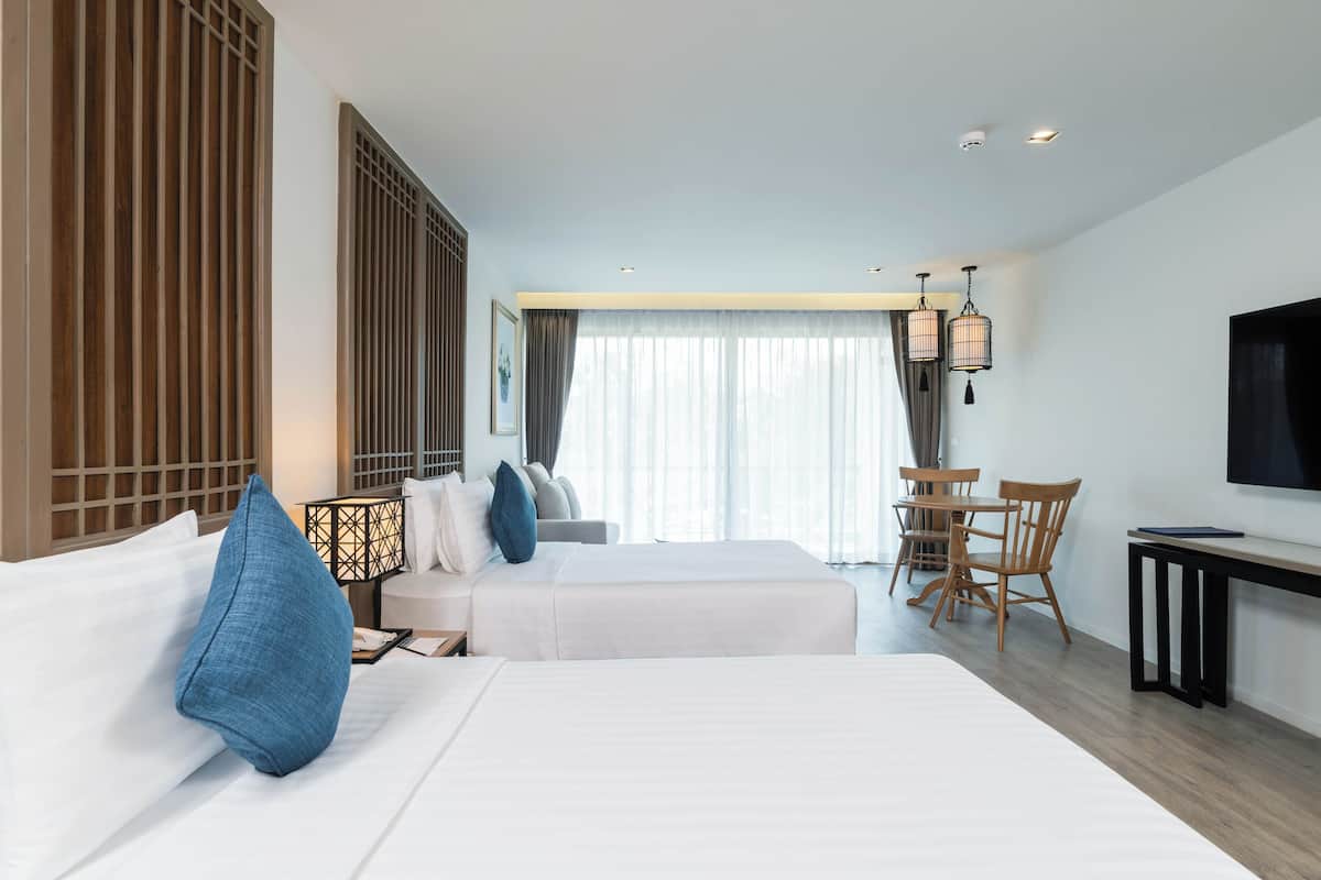 A hotel room with two beds, a desk, a TV, and a dining area.