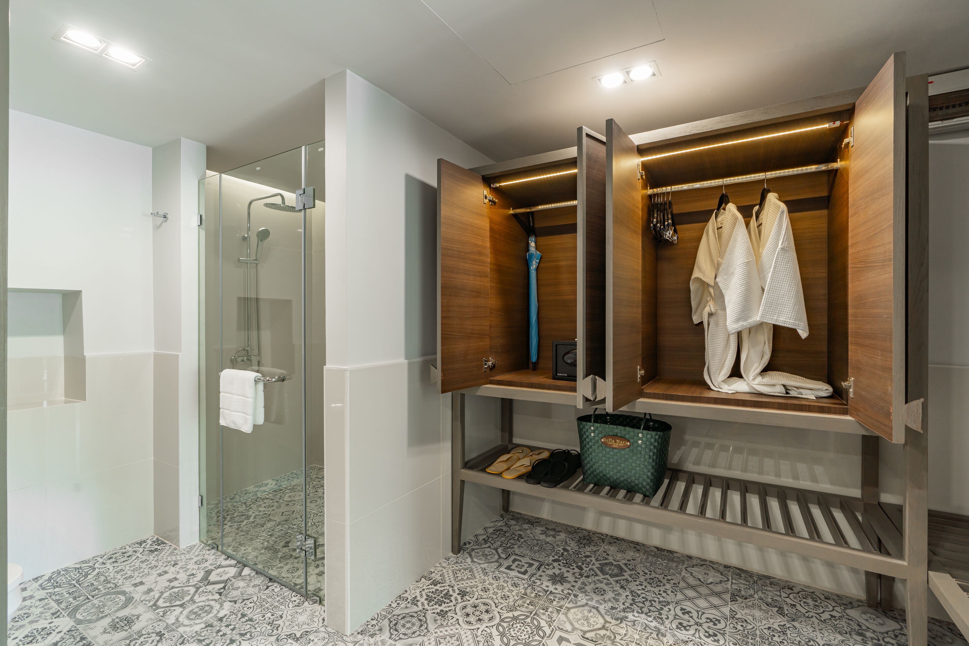 A modern bathroom with a glass-enclosed shower, a wooden vanity with a towel rack, and patterned floor tiles.