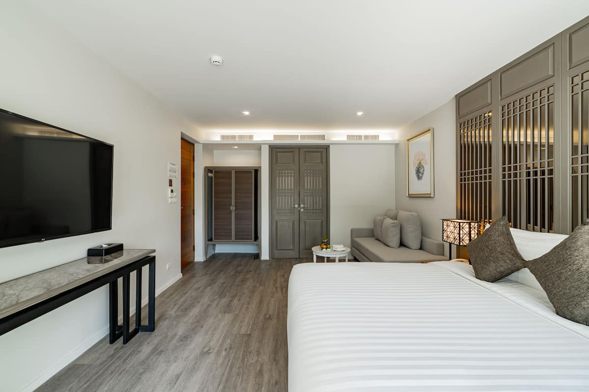 A modern hotel room with a large bed, a TV, a desk, a sofa, and a wardrobe.