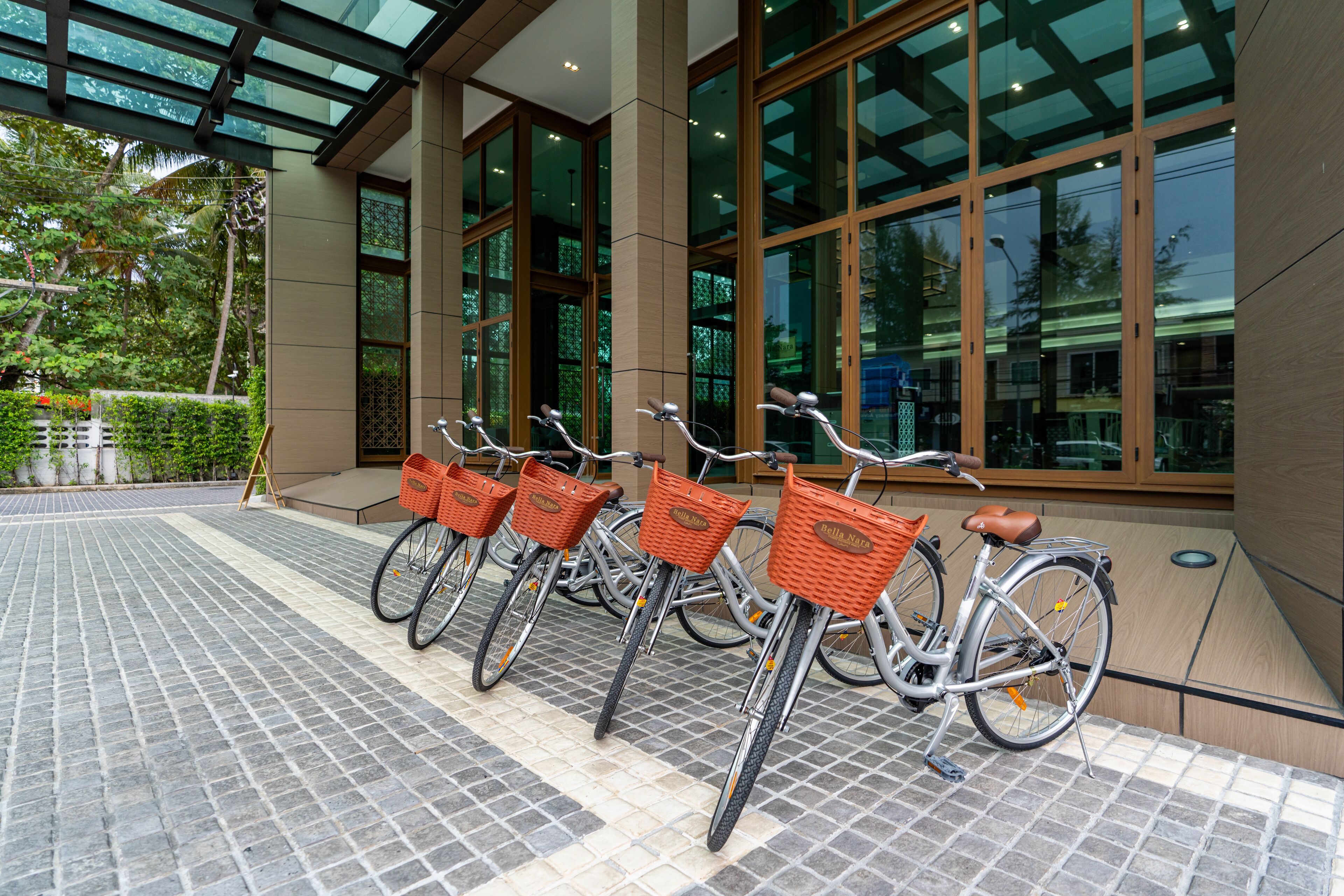 Varias bicicletas con cestas estacionadas frente a un edificio con amplias ventanas.