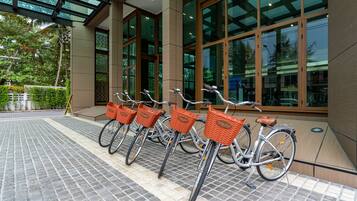 Varias bicicletas con cestas estacionadas frente a un edificio con amplias ventanas.