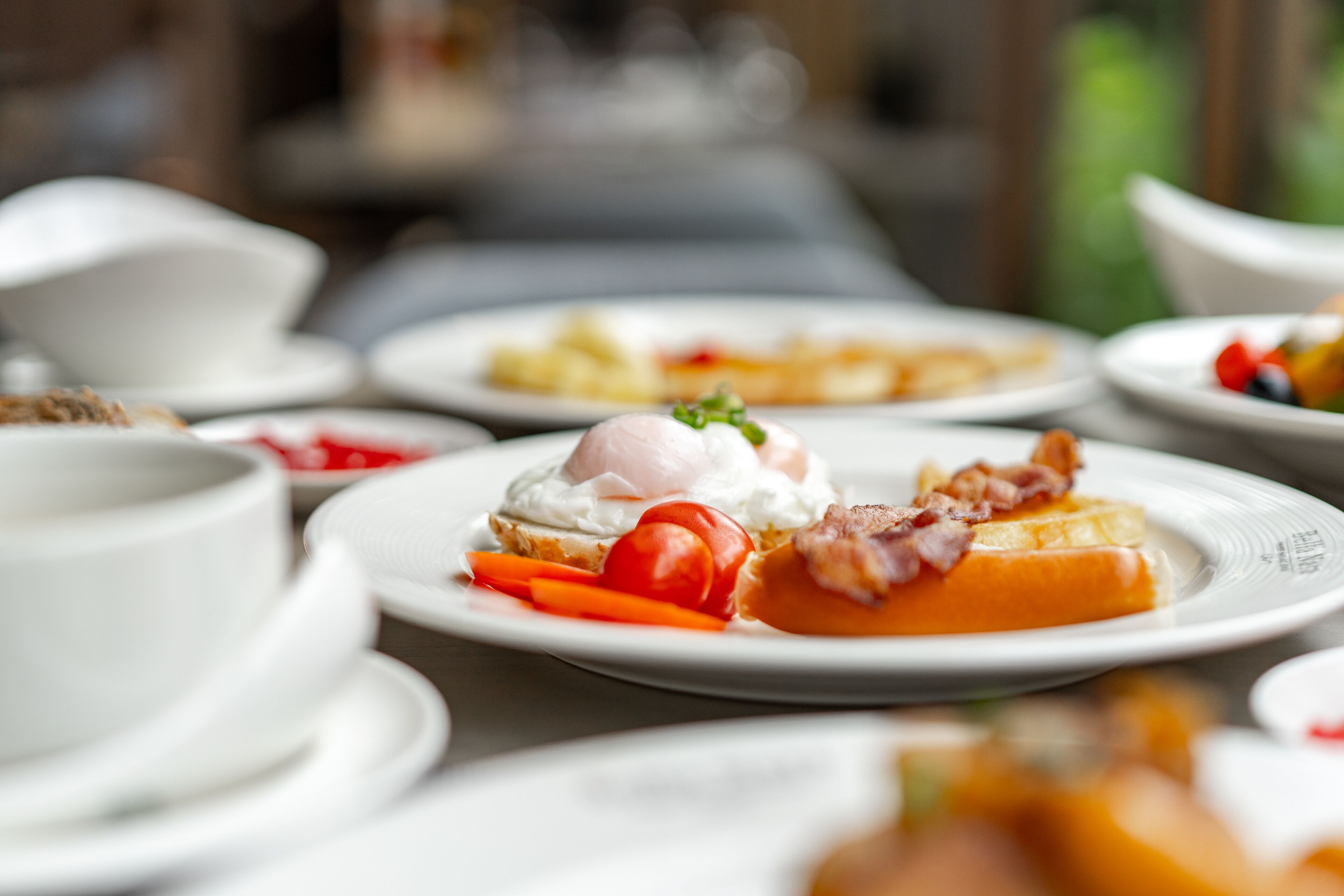 A dining table with various plates of food, including a poached egg on toast, tomatoes, and bacon.