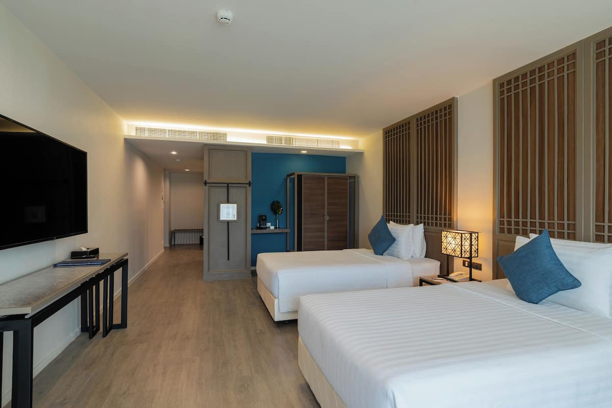 A hotel room with two beds, a TV, a desk, and a bathroom.
