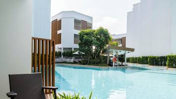 Zona junto a la piscina con mobiliario de mimbre y vista a un conjunto de edificios.