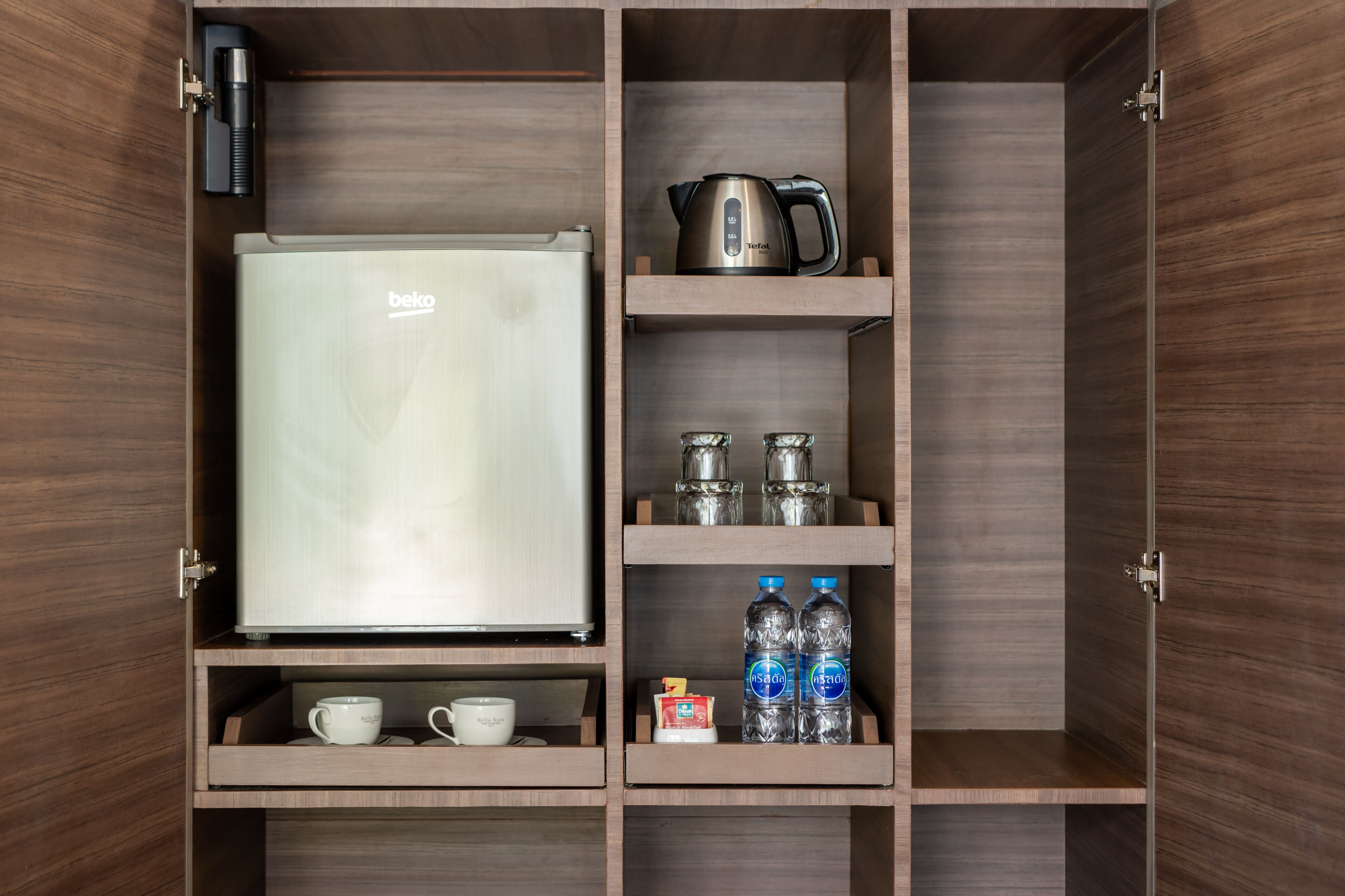 Un minibár con un refrigerador, una tetera, dos tazas, dos botellas de agua y una pequeña caja.