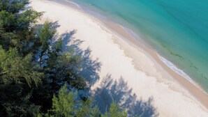 A beach with clear turquoise water and sandy shore, surrounded by dense green foliage. - Bella Nara Phuket Naiyang Beach (Sa Khu)