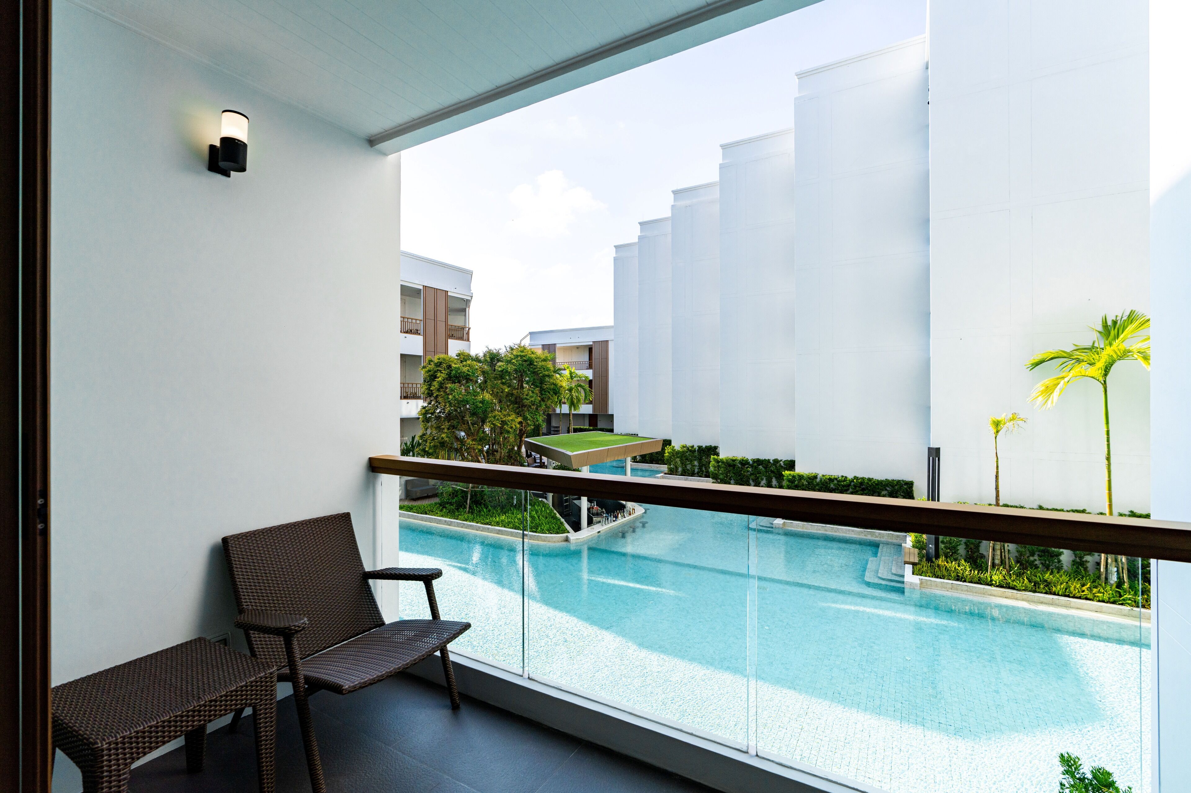 A balcony with a view of a swimming pool, a lounge chair, and a small table.