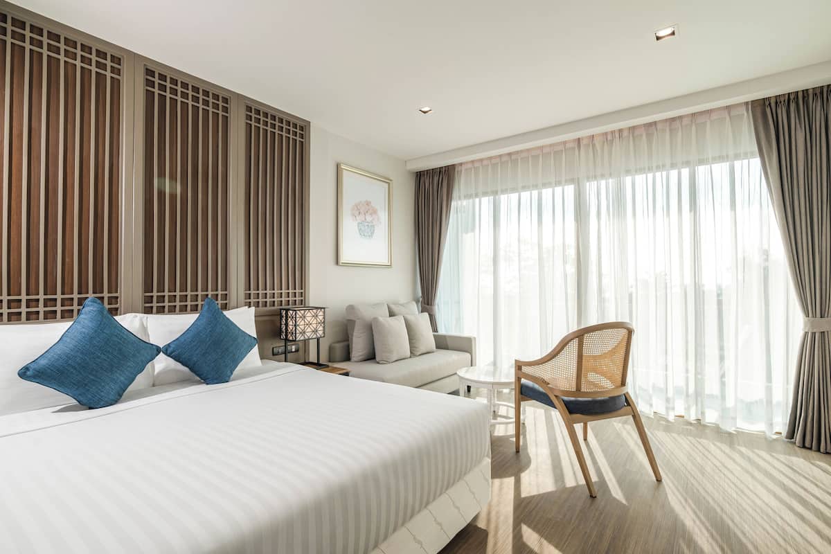 A hotel room with a large bed, a sofa, a chair, and a desk.