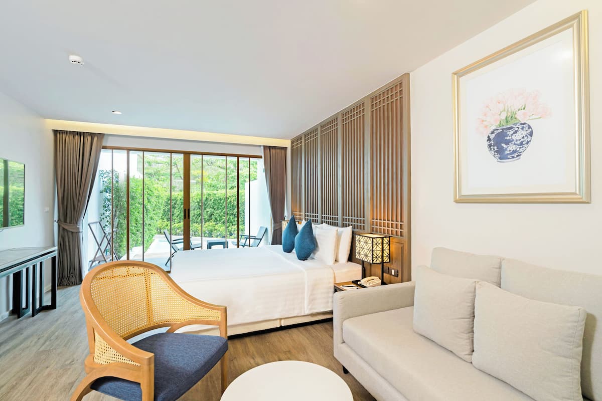 A hotel room with a bed, a sofa, a chair, a desk, and a window with curtains.