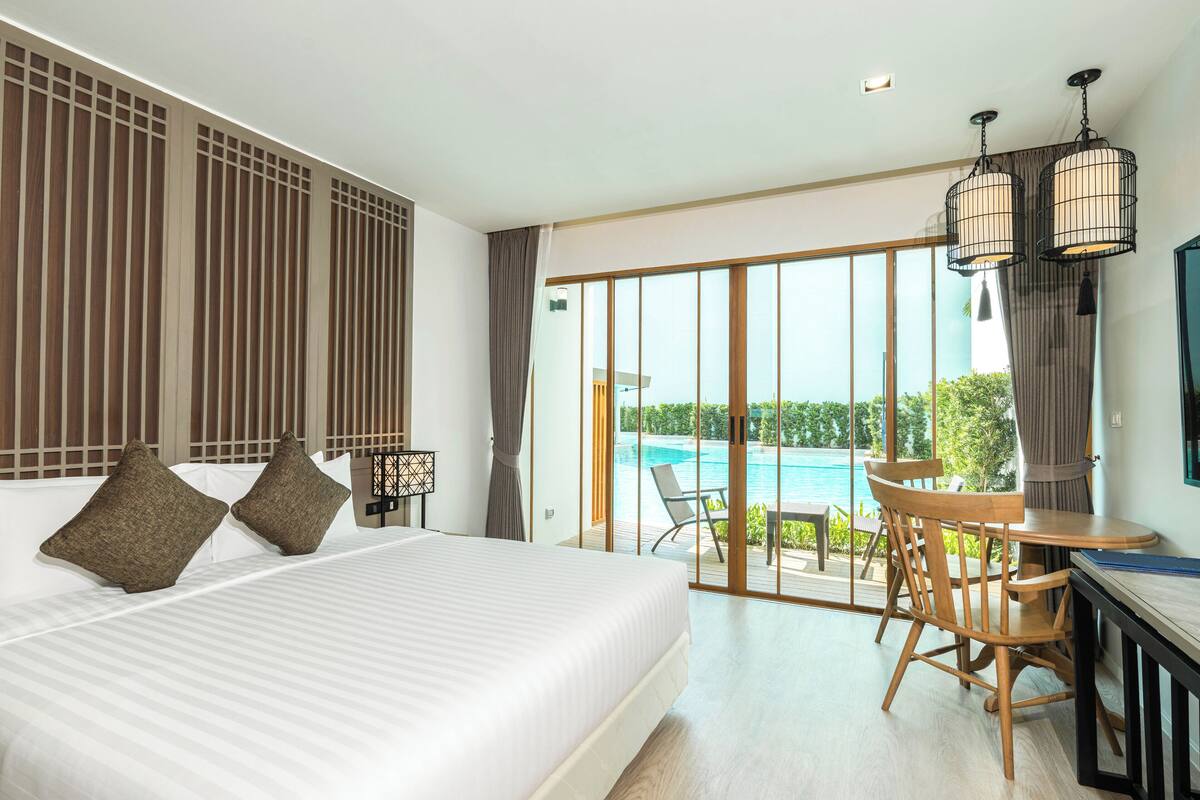 A hotel room with a large bed, a dining table with chairs, and a view of a swimming pool.