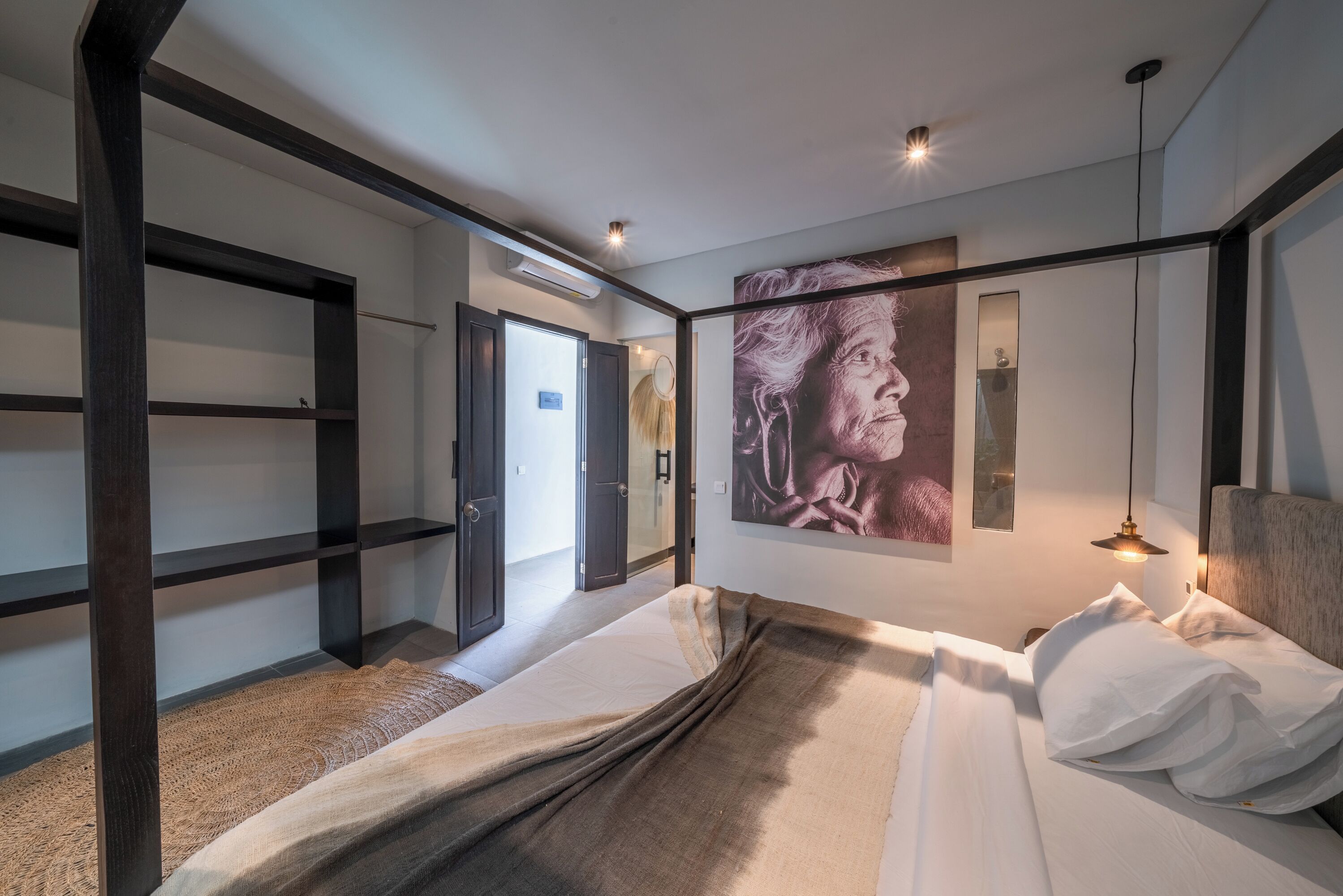 A modern hotel room with a bed, a large wall painting, a mirror, and a door leading to another room.