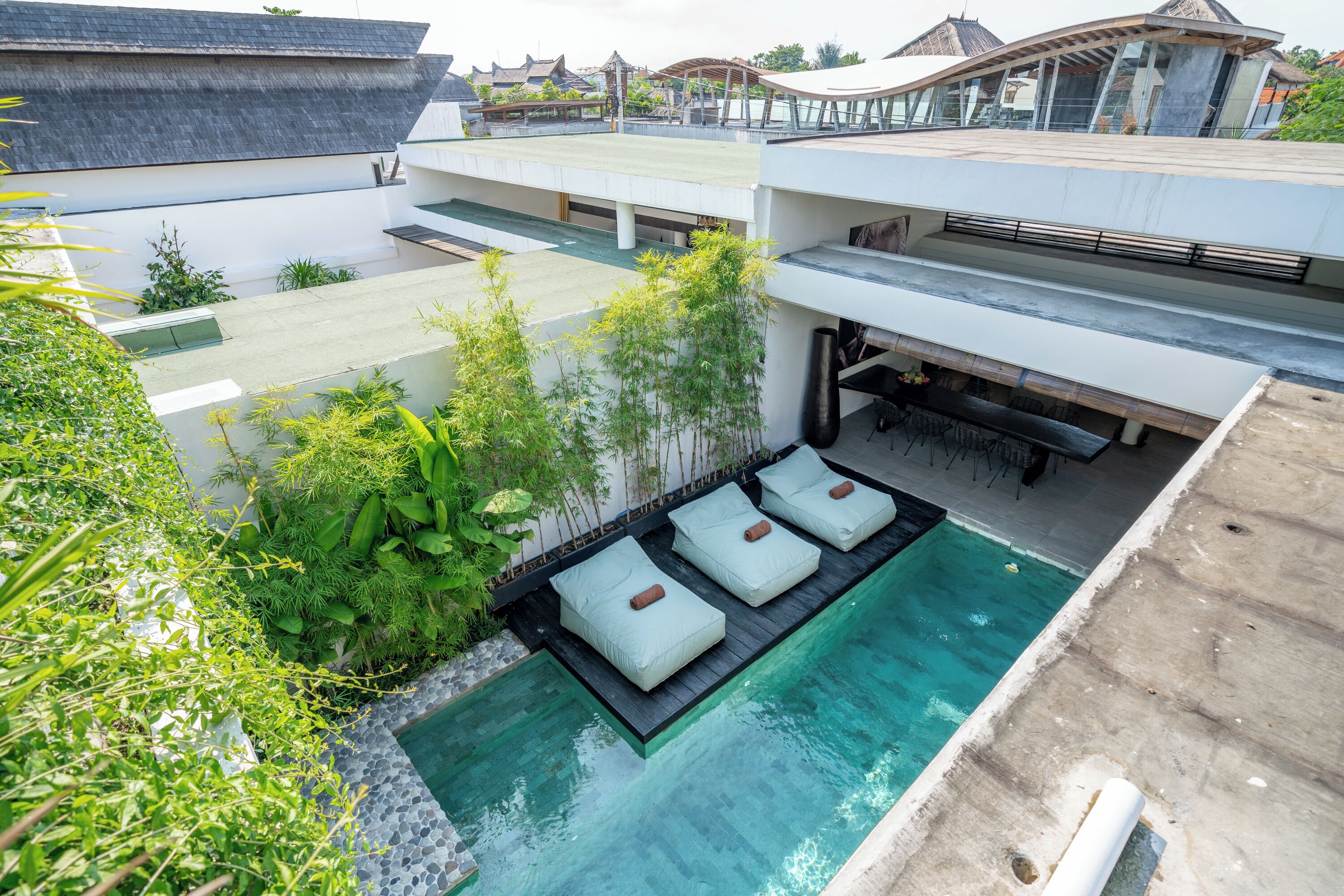 A rooftop pool with three lounge chairs and a small waterfall feature.