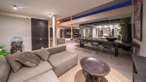 A modern living room with a sectional sofa, a round coffee table, and a dining area with a large table and chairs. - Villa Wiraja 2 (Canggu)