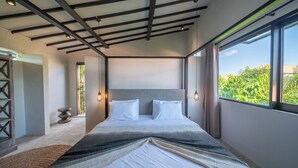 A modern bedroom with a large bed, a view of greenery outside, and a unique ceiling design. - Villa Wiraja 2 (Canggu)