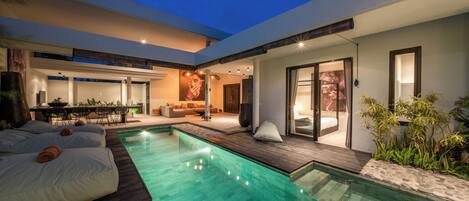 Un espace piscine extérieur moderne, doté d’une terrasse en bois, de chaises longues et d’un coin repas avec une table et des chaises.